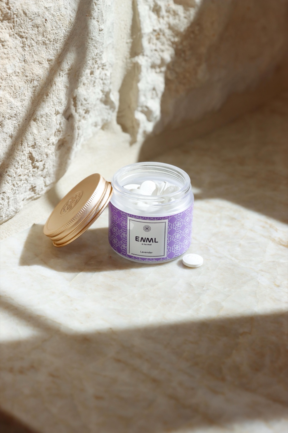 An open jar of ENML fluoride-free toothpaste tablets on travertine stone